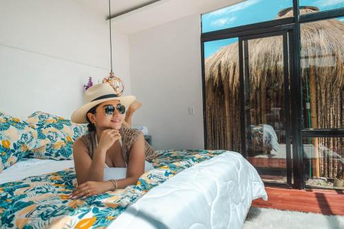 Una donna sdraiata su un letto con un cappello e degli occhiali da sole di Mirador del Magdalena Hotel y Glamping a Isnos