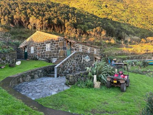 a stone house with a tractor in front of it at Caldeira Guesthouse in Fajã da Caldeira de Santo Cristo