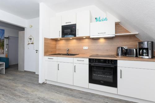 a kitchen with white cabinets and black appliances at Haus Strandkorb mit Frühstücksoption in Bensersiel