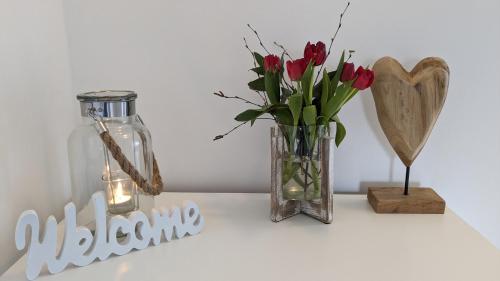 eine Vase mit roten Rosen und einem Herz und einem Aason-Glas in der Unterkunft FeWo Catalina in Westerstede