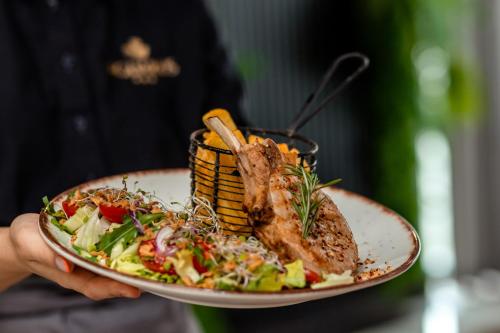 a person holding a plate of food with meat and salad at Hotel Aquarius Restaurant Wellness Spa in Ciechocinek