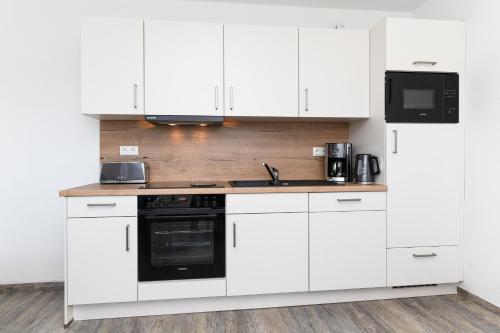 a white kitchen with white cabinets and a black appliance at Haus Strandkorb mit Frühstücksoption in Bensersiel