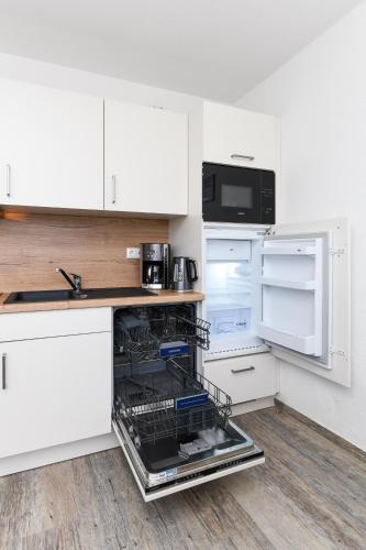 an open dishwasher in a kitchen with white cabinets at Haus Strandkorb mit Frühstücksoption in Bensersiel