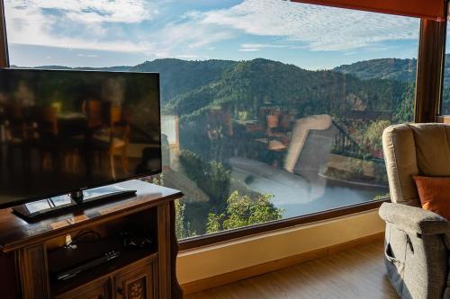 een woonkamer met een tv en een groot raam bij Casa El Mirador del Miño en la Ribeira Sacra in Rosende