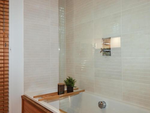 a bathroom with a tub and a shower with white tiles at 1 Streamside in Looe
