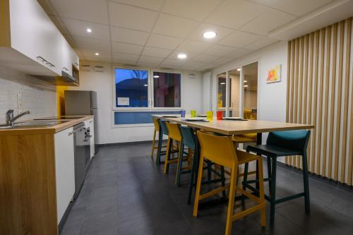 une cuisine avec une grande table et des chaises jaunes dans l'établissement Résidence Nemea Gières Campus, à Gières