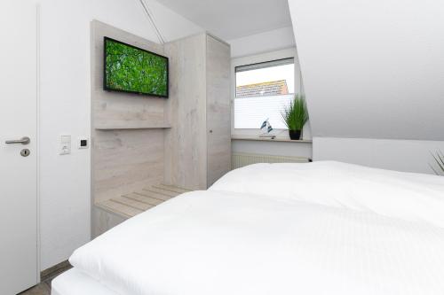 a bedroom with a white bed and a flat screen tv at Haus Strandkorb mit Frühstücksoption in Bensersiel