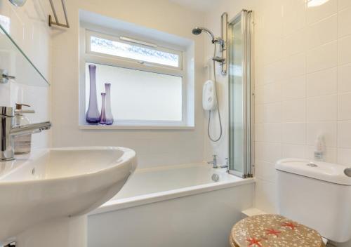 a white bathroom with a sink and a tub and a window at Gone To The Beach - Fishcombe Cove in Brixham