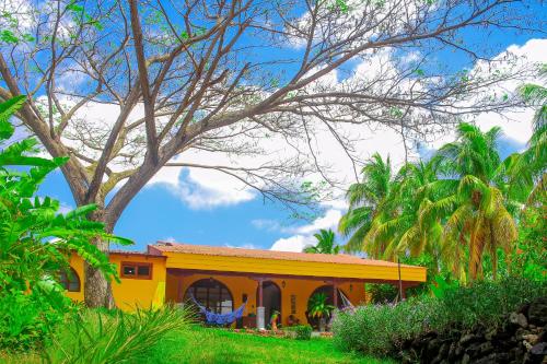 a yellow house with a tree in the foreground at Hotel Amigo Nicaragua in Nindirí