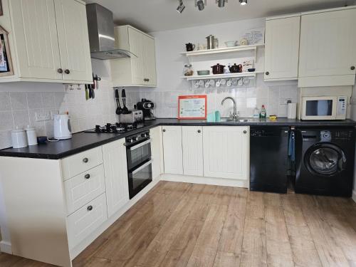 a kitchen with white cabinets and a black dishwasher at Bespoke coastal 2 bed cottage with free parking in Ilfracombe