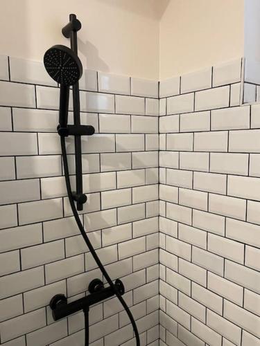 - une douche carrelée de blanc avec un pommeau de douche noir dans l'établissement Le Bubble, à Épernay