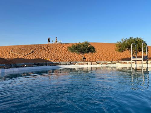 a pool of water with people standing on a hill at Sahara Majestic Luxury Camp in Merzouga