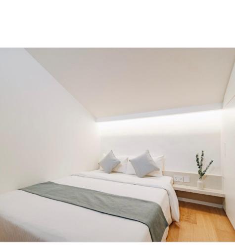 um quarto branco com uma cama com lençóis e almofadas brancos em Social-Inn Norris Road Apt em Singapura