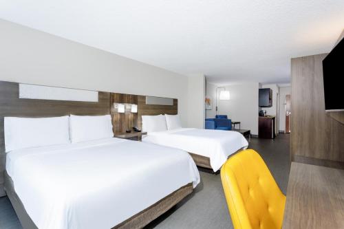 a hotel room with two beds and a yellow chair at Holiday Inn Express & Suites Jacksonville - Atlantic Beach by IHG in Jacksonville