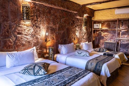 2 camas en una habitación con una pared de piedra en Hotel Xaluca Dades en Boumalne