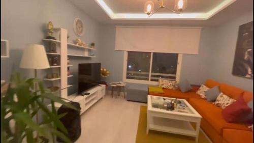 Happiness Place في King Abdullah Economic City: غرفة معيشة مع أريكة برتقالية وتلفزيون