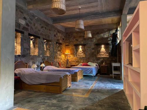 1 dormitorio con 2 camas y pared de piedra en La Llama Negra en Tilcara