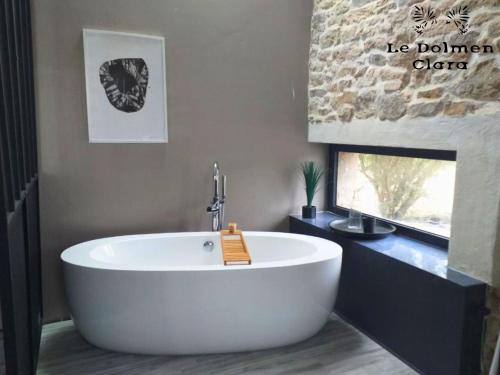 a white bath tub in a bathroom with a stone wall at Le Loft du Dolmen Clara, entre terre et mer in Plounévez-Lochrist