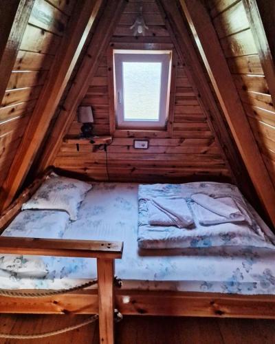 an attic bed in a wooden house with a window at Durmitorski konaci apartments in Žabljak