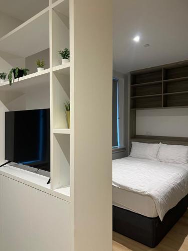 a bedroom with a bed and a tv and shelves at London Heathrow Airport Apartment Voyager House Terminal 12345 - EV Electric and Parking available! in New Bedfont