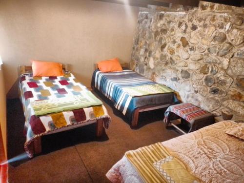 a room with two beds and a stone wall at HOSTEL SAMANA WASI CHAULLAY in Colcapampa