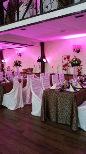 a room with tables and white chairs and pink lighting at Hamlet Hotel in Bacău