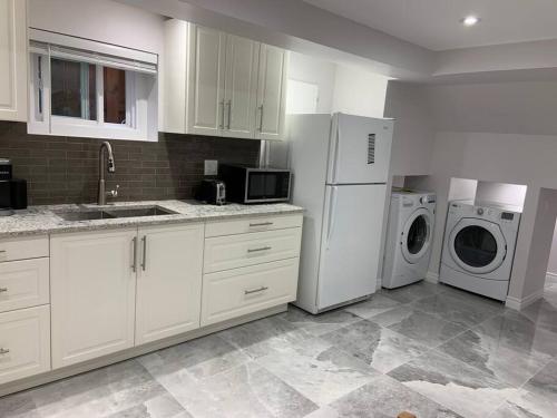 a kitchen with white cabinets and a washer and dryer at Luxurious brand new ground level apartment in Mississauga
