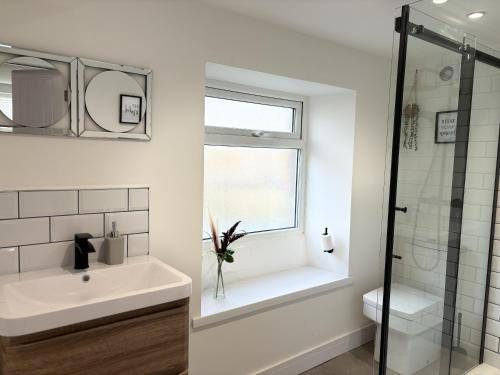 ein weißes Bad mit einem Waschbecken und einem Fenster in der Unterkunft Hardy Hideaway in Ulverston