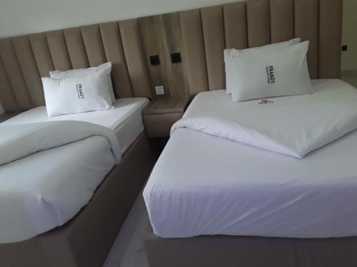 2 bedden in een hotelkamer met witte lakens en kussens bij Franzy Luxury Hotel & Suites in Jos