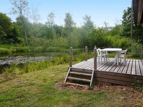 einen Tisch und einen Stuhl auf einer Holzterrasse neben einem Teich in der Unterkunft 4 person holiday home in SMEDSTORP in Smedstorp