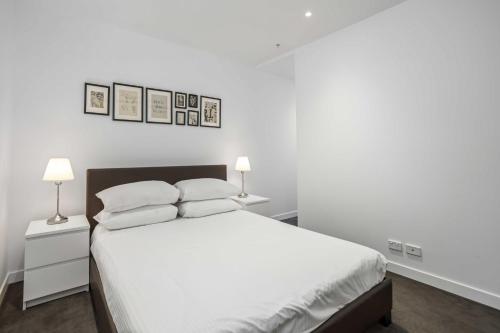 a white bedroom with a bed and three pictures on the wall at Chic 1-Bed with Parking, Rooftop Pool and Gym in Brisbane