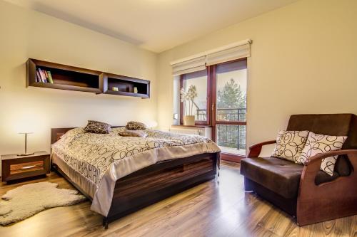 a bedroom with a bed and a chair and a window at Apartament Storczyk Zakopane in Zakopane