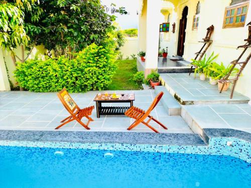 eine Terrasse mit 2 Stühlen und einem Tisch neben einem Pool in der Unterkunft The heavens villa udaipur in Udaipur