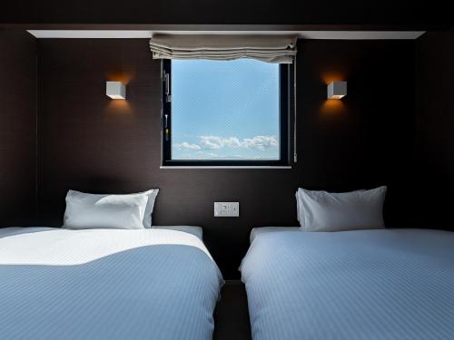 two beds in a room with a window at Kaname Inn Tatemachi in Kanazawa