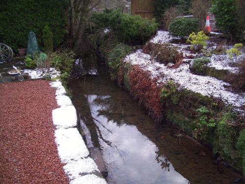 a stream in a garden with snow on the ground at The Old Smiddy Cottage and Apartment in Balloch