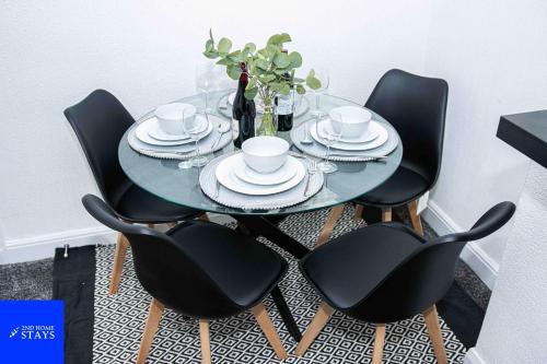 a dining room table with black chairs and a glass table with plates at 2ndHomeStays- Stoke-on-Trent-A Serene 3 Bed House with a Garden View-Suitable for Contractors-Relocation Families-Group of Friends-Sleeps 6 - 16 mins to J15 M6 and 36 mins to Alton Towers Resort in Stoke on Trent