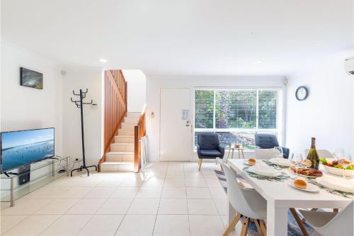 a white living room with a table and a tv at 1 75 Rocky Point Road fantastic holiday home with in Fingal Bay