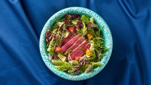 a bowl of salad with meat and vegetables on a blue table at Crowne Plaza Changi Airport by IHG in Singapore