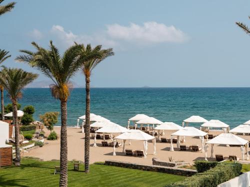 a beach with white umbrellas and the ocean at Amirandes, A Grecotel Resort to Live in Gouves