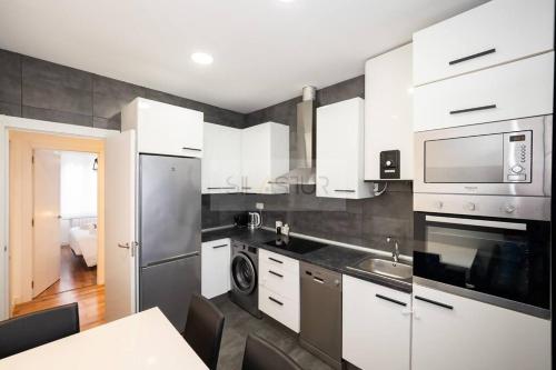 una cocina con armarios blancos y electrodomésticos de acero inoxidable en Vive Oviedo II Apartamento, en Oviedo