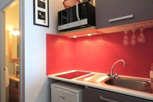 - une cuisine rouge avec évier et four micro-ondes dans l'établissement Studio VUE SUR MER sur la plage de Trestrignel à PERROS-GUIREC - Réf 833, à Perros-Guirec