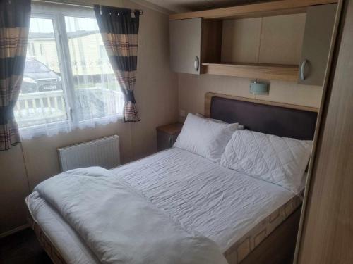 a bed in a small room with a window at 8 BERTH Deluxe caravan PALM GROVE 142 GOLDEN PALM CHAPEL ST LEONARDS in Chapel Saint Leonards
