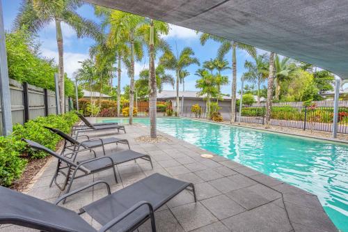 a swimming pool with chairs and palm trees at Nature View Southside Apartment in Cairns
