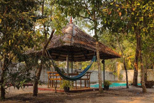 una hamaca en una cabaña con 2 sillas y un árbol en RIVA Marari Beach Homestay, en Mararikulam