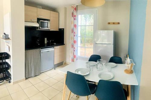 Il comprend une cuisine avec une table et des chaises blanches ainsi qu'une cuisine équipée d'un réfrigérateur. dans l'établissement Hélice - Maison sous les pins, à Longeville-sur-Mer