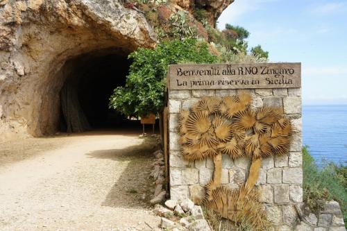 a sign in front of a cave next to the ocean at Dentro Scopello - Casa Vacanze in Scopello