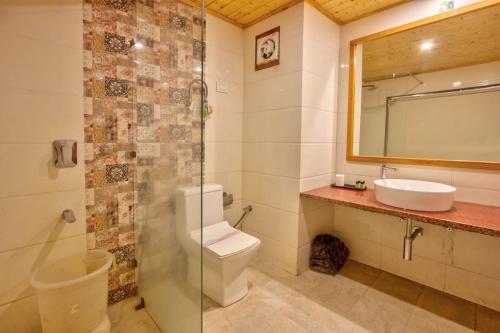 a bathroom with a toilet and a sink and a mirror at Hotel Grand Oasis in Manāli