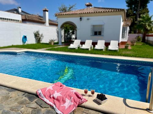 a swimming pool with a towel and drinks next to a house at Chalet Manku in Chiclana de la Frontera