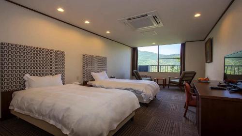 箱根町にある海悦温泉ホテルのベッド2台、デスク、窓が備わるホテルルームです。