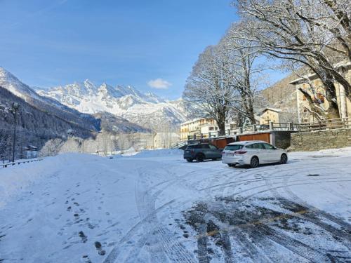 two cars parked on a snow covered street with mountains at Grand Hotel Ceresole Reale studio apartment in Ceresole Reale